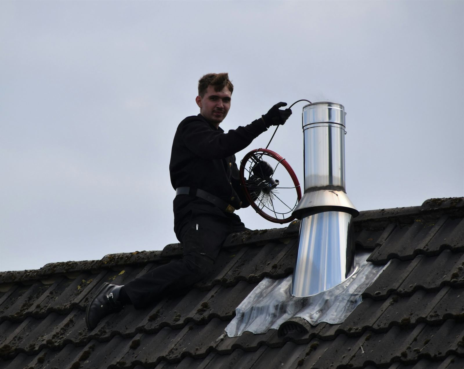 Ramoneur sur un toit, hérisson à la main, au-dessus du conduit
